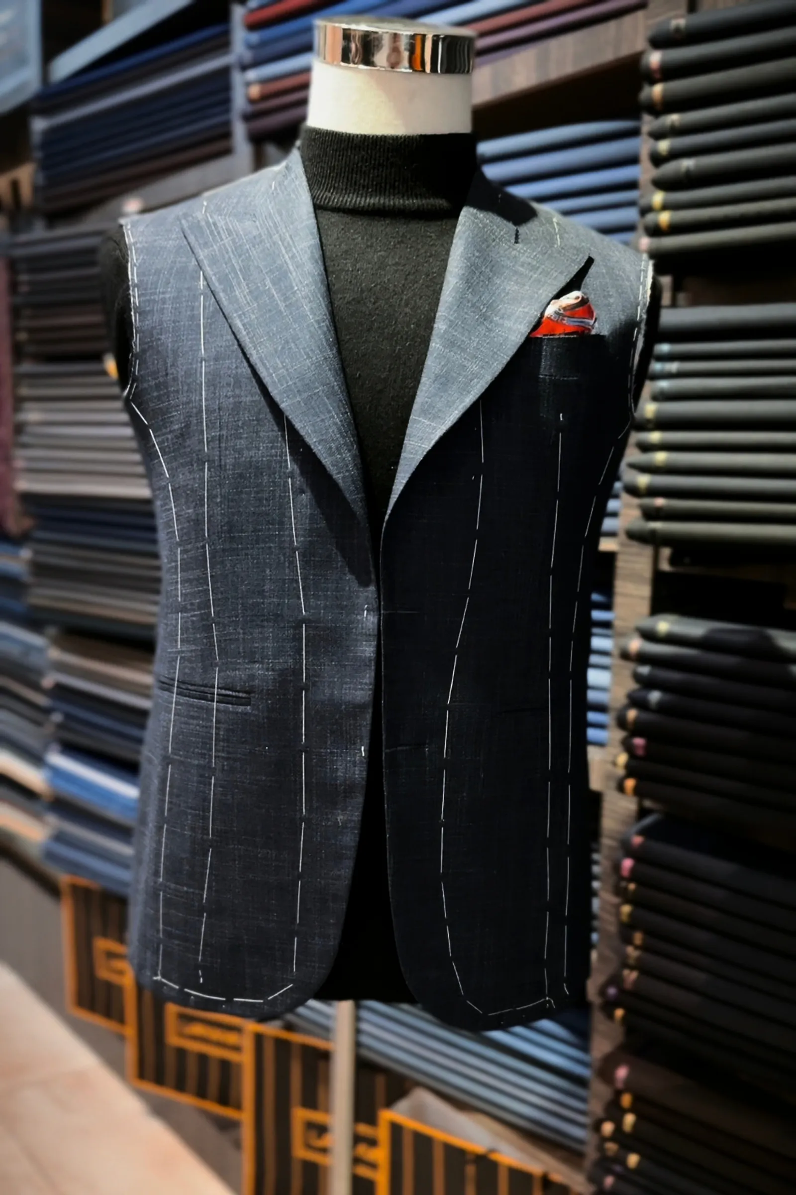 Basted bespoke jacket on a tailor's form in front of cloth shelves